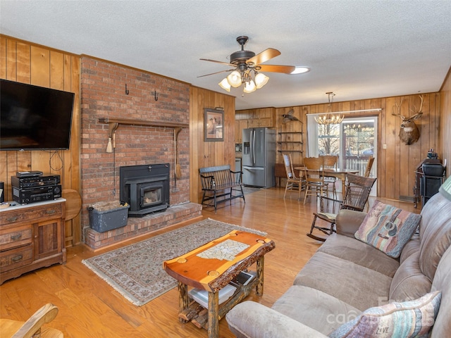 living room with ceiling fan with notable chandelier, wood walls, a textured ceiling, and light hardwood / wood-style flooring