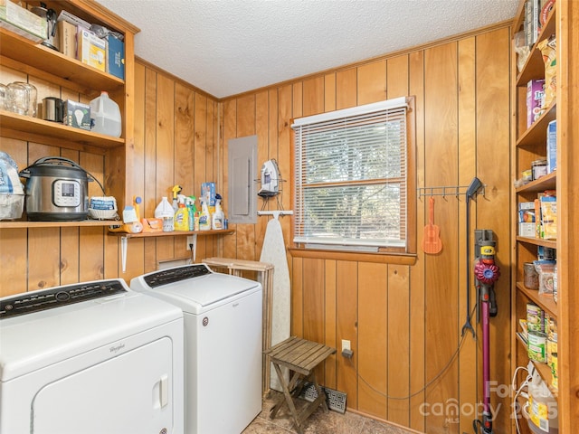 laundry room with wooden walls, electric panel, washer and dryer, and a textured ceiling