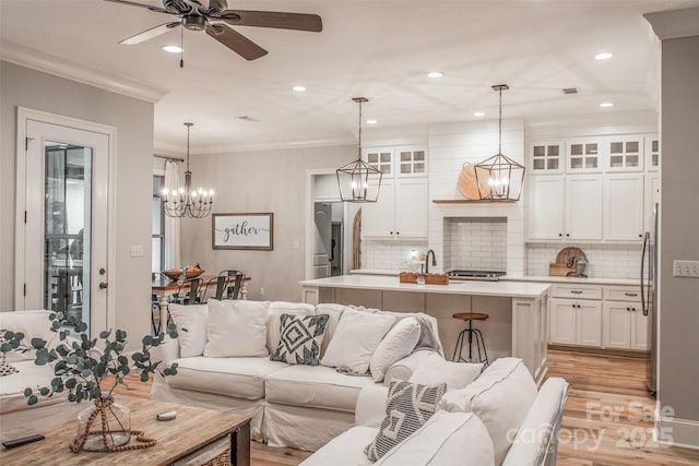 living room featuring ornamental molding, sink, ceiling fan with notable chandelier, and light hardwood / wood-style floors