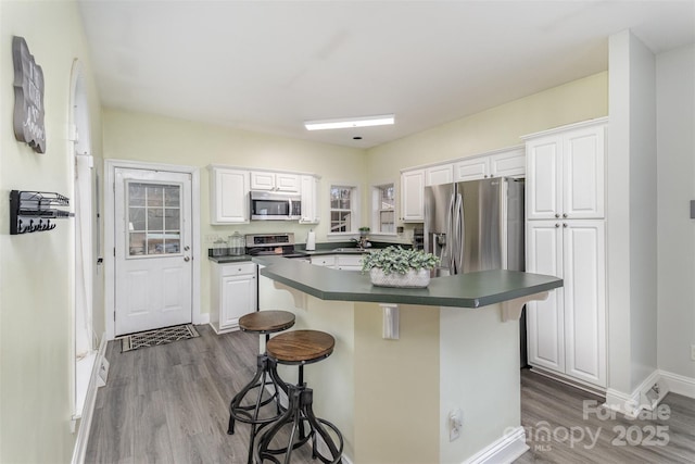 kitchen with a breakfast bar area, white cabinetry, wood-type flooring, appliances with stainless steel finishes, and a kitchen island