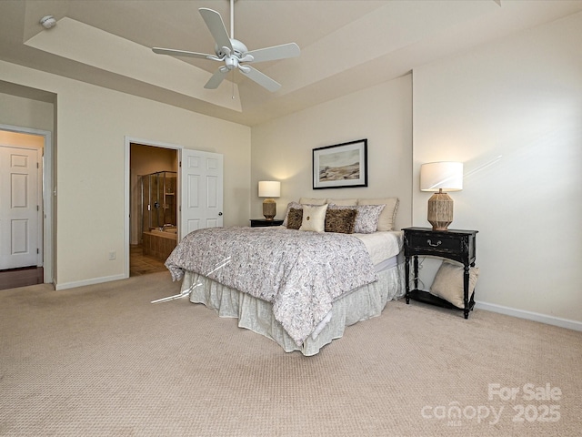 bedroom with light carpet, connected bathroom, a tray ceiling, and ceiling fan