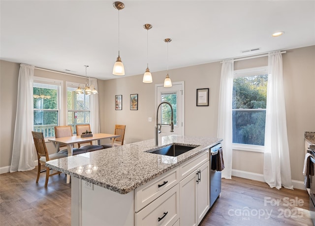 kitchen featuring sink, white cabinets, hanging light fixtures, a kitchen island with sink, and light stone counters