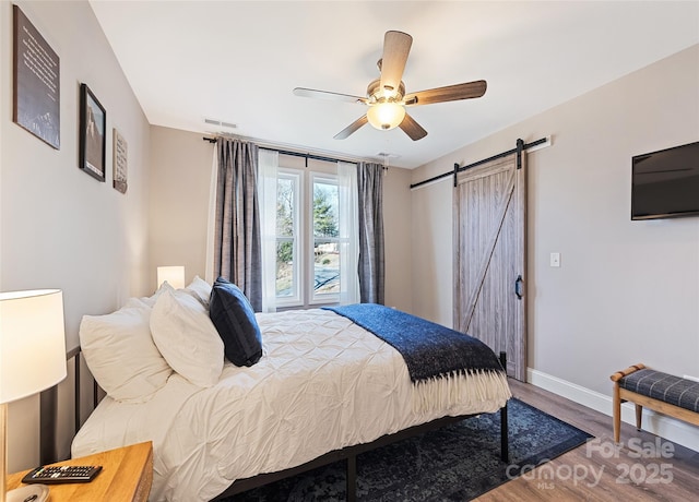 bedroom featuring wood-type flooring, a barn door, and ceiling fan