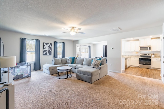 living room featuring a textured ceiling, light colored carpet, and ceiling fan