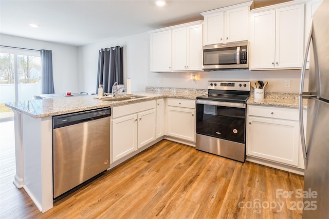 kitchen with light stone counters, stainless steel appliances, kitchen peninsula, and white cabinets