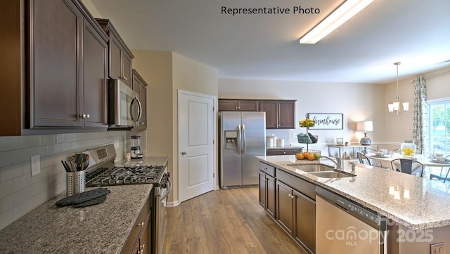 kitchen featuring an island with sink, a sink, wood finished floors, stainless steel appliances, and light stone countertops