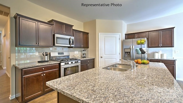 kitchen featuring light wood-style flooring, a sink, decorative backsplash, stainless steel appliances, and dark brown cabinets