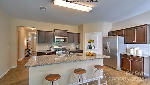 kitchen with dark brown cabinets, stainless steel appliances, light wood-type flooring, and a sink