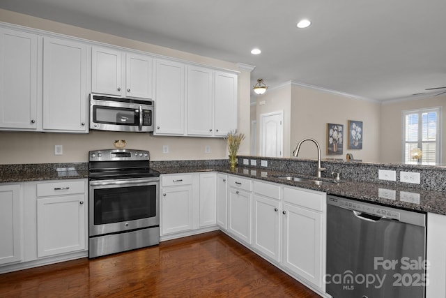 kitchen with crown molding, appliances with stainless steel finishes, white cabinetry, a sink, and dark stone countertops