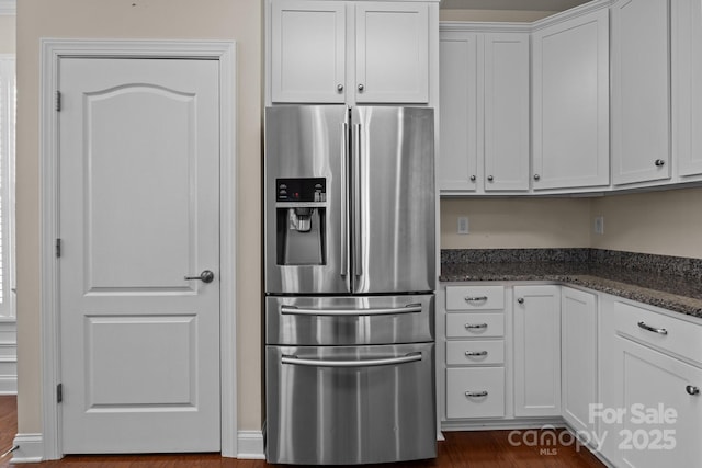 kitchen featuring dark stone counters, stainless steel refrigerator with ice dispenser, and white cabinetry