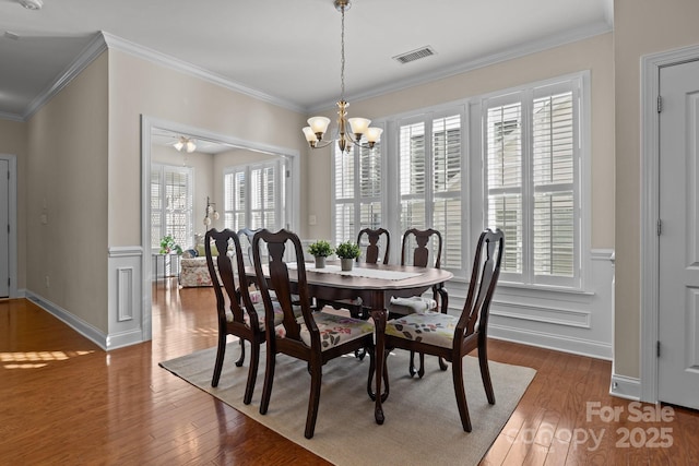 dining room featuring a notable chandelier, visible vents, a decorative wall, ornamental molding, and hardwood / wood-style floors