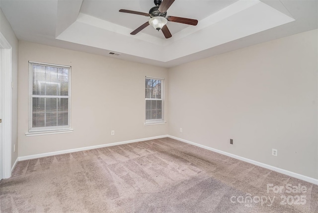 carpeted empty room with a raised ceiling and ceiling fan