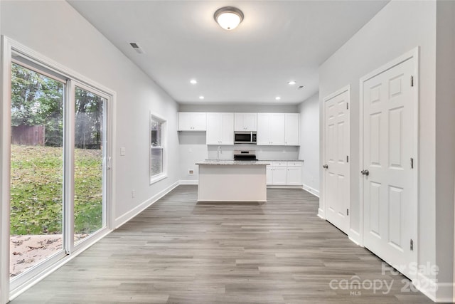 kitchen with stove, hardwood / wood-style floors, light stone counters, white cabinets, and a kitchen island