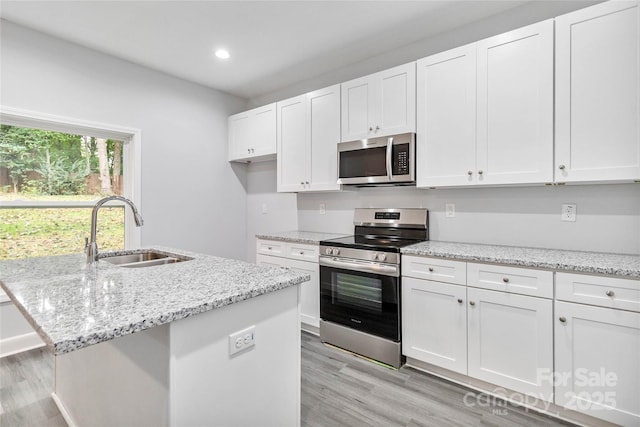 kitchen with sink, white cabinetry, stainless steel appliances, light stone countertops, and a kitchen island with sink