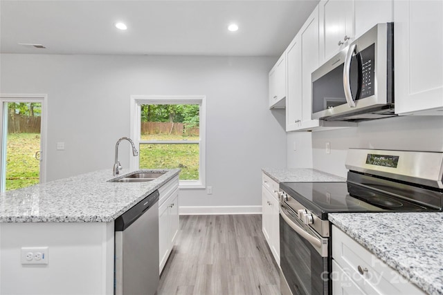 kitchen featuring appliances with stainless steel finishes, white cabinetry, an island with sink, sink, and light hardwood / wood-style flooring