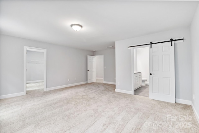 unfurnished bedroom featuring ensuite bath, a walk in closet, a closet, light colored carpet, and a barn door