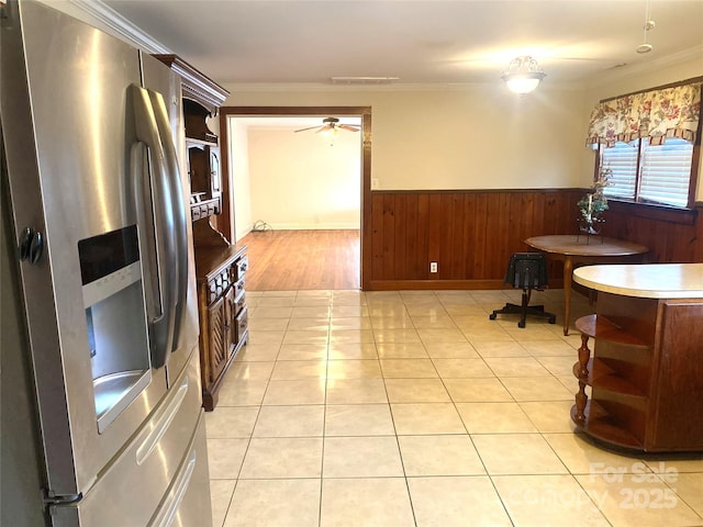 kitchen with light tile patterned flooring, ornamental molding, stainless steel fridge with ice dispenser, and wood walls