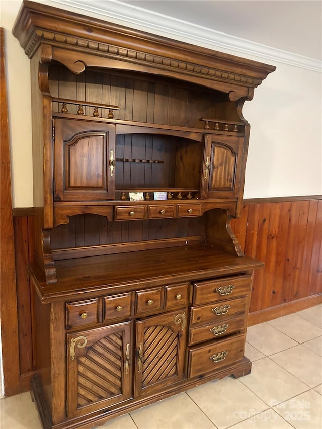 bar featuring crown molding, dark brown cabinetry, light tile patterned floors, and wood walls