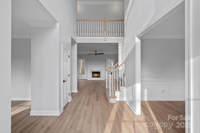 entrance foyer featuring crown molding, a towering ceiling, ceiling fan, and light wood-type flooring