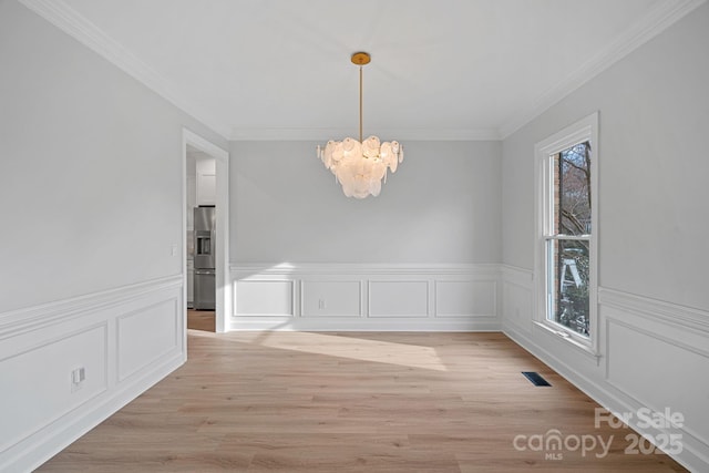 unfurnished dining area with ornamental molding, a chandelier, and light wood-type flooring