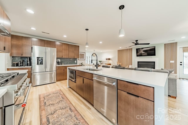 kitchen with sink, high end appliances, light hardwood / wood-style flooring, a center island with sink, and pendant lighting