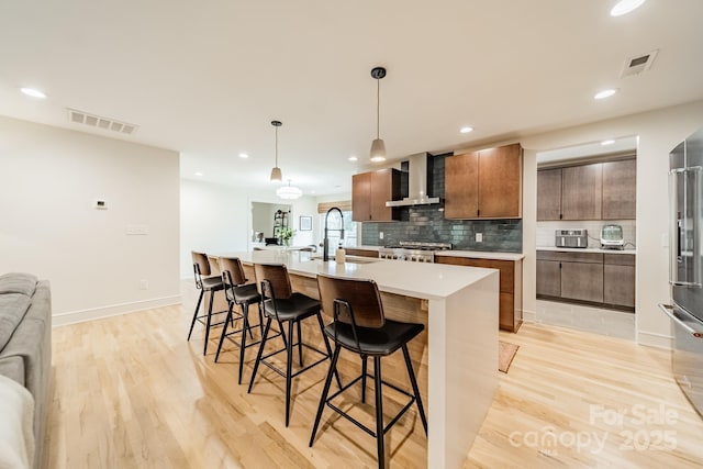 kitchen with light countertops, wall chimney range hood, an island with sink, and a sink