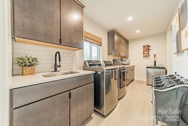 clothes washing area featuring recessed lighting, a sink, baseboards, washer and dryer, and cabinet space