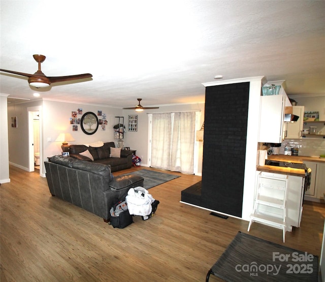 living room featuring crown molding, wood-type flooring, and ceiling fan