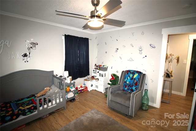 bedroom featuring crown molding, a nursery area, hardwood / wood-style floors, and ceiling fan