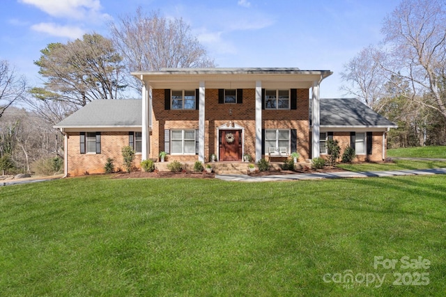 greek revival house featuring brick siding, roof with shingles, and a front yard