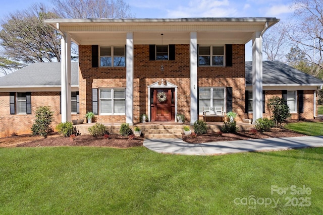 neoclassical home featuring a front lawn, a shingled roof, and brick siding