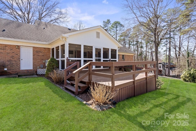 rear view of property with brick siding, a shingled roof, a sunroom, a yard, and a wooden deck