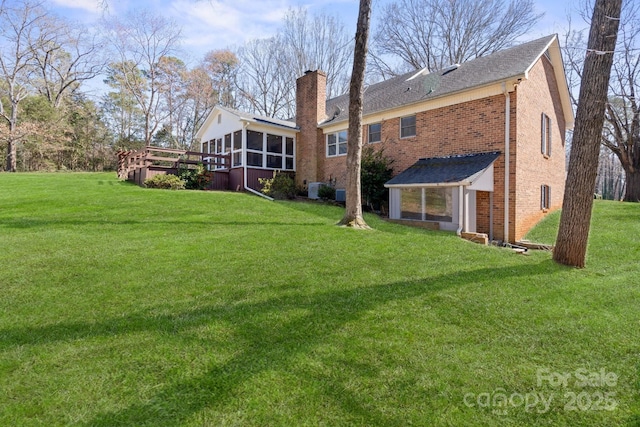 rear view of property with a lawn, brick siding, a chimney, and a sunroom