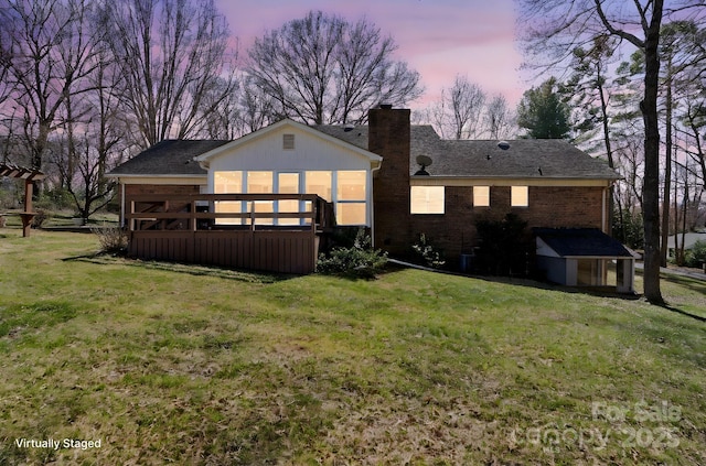 rear view of property featuring a deck, brick siding, a lawn, and a chimney