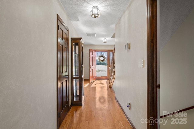 hall featuring baseboards, visible vents, a textured ceiling, and light wood finished floors