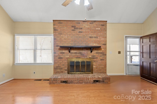 unfurnished living room featuring vaulted ceiling, a brick fireplace, plenty of natural light, and wood finished floors