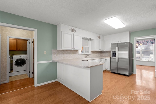 kitchen featuring stainless steel refrigerator with ice dispenser, light wood-style flooring, white cabinets, washer / dryer, and a peninsula