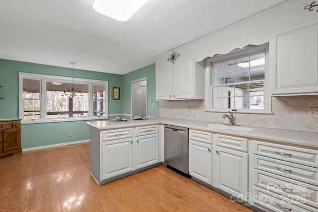 kitchen with light countertops, stainless steel dishwasher, white cabinets, a sink, and a peninsula