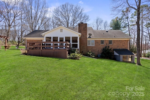 back of property with a deck, brick siding, a yard, and a chimney