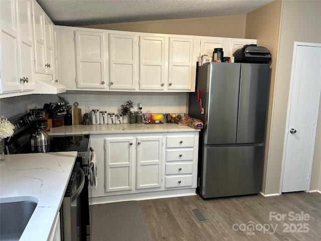 kitchen with dark wood-type flooring, lofted ceiling, range with electric stovetop, stainless steel refrigerator, and white cabinets