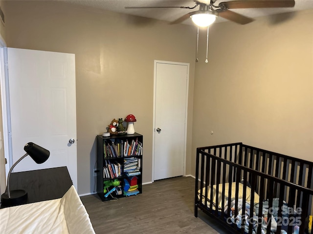 bedroom with a crib, dark hardwood / wood-style floors, and ceiling fan