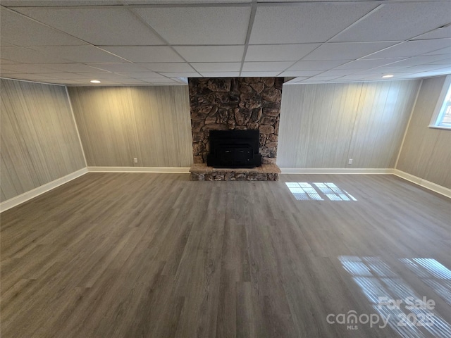 basement featuring hardwood / wood-style floors, a drop ceiling, a fireplace, and wood walls