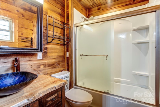 full bathroom featuring toilet, vanity, shower / bath combination with glass door, and wood walls