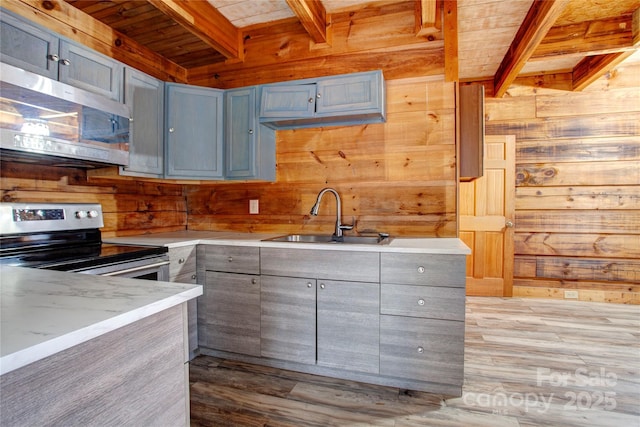 kitchen with beamed ceiling, stainless steel appliances, sink, and wood walls