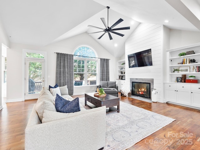 living room with light hardwood / wood-style flooring, built in shelves, a fireplace, and ceiling fan