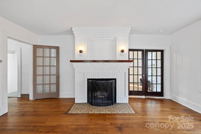 unfurnished living room with hardwood / wood-style flooring, crown molding, a brick fireplace, and french doors