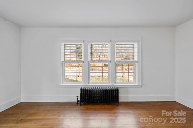 unfurnished room featuring wood-type flooring, plenty of natural light, and radiator