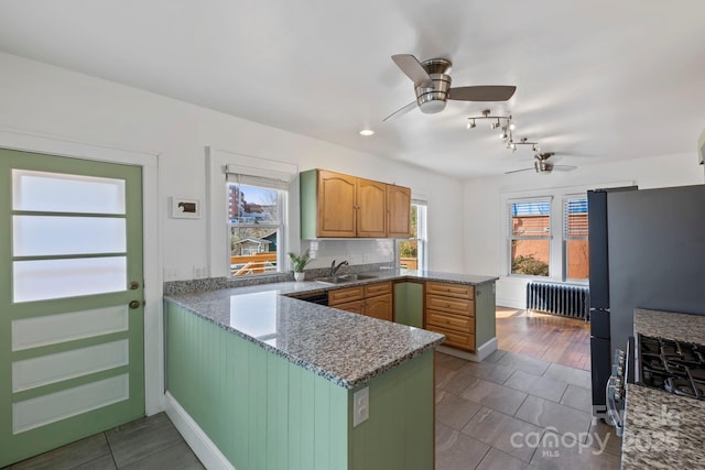 kitchen featuring radiator, sink, stainless steel refrigerator, dark stone countertops, and kitchen peninsula