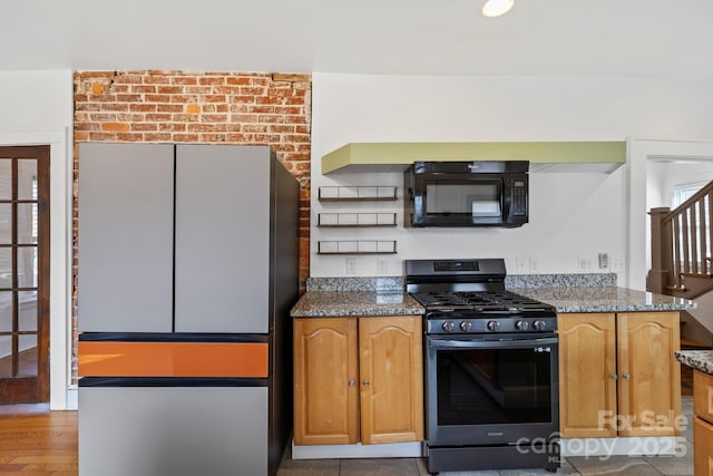 kitchen featuring fridge, dark stone countertops, and stainless steel gas range