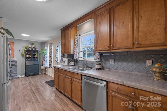 kitchen with appliances with stainless steel finishes, tile counters, sink, and backsplash